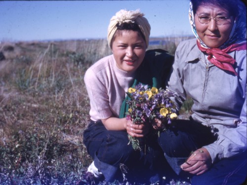 Vintage color photograph of two women kneeling down in a field holding a bouquet of flowers.